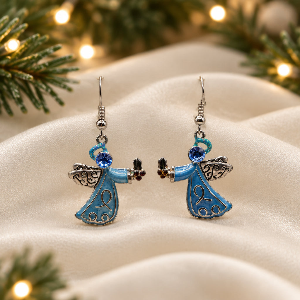 A pair of dangling angel earrings with light blue enamel bodies, silver-toned wings and hooks, and small dark bead accents, displayed on a clear stand against a light gray background.