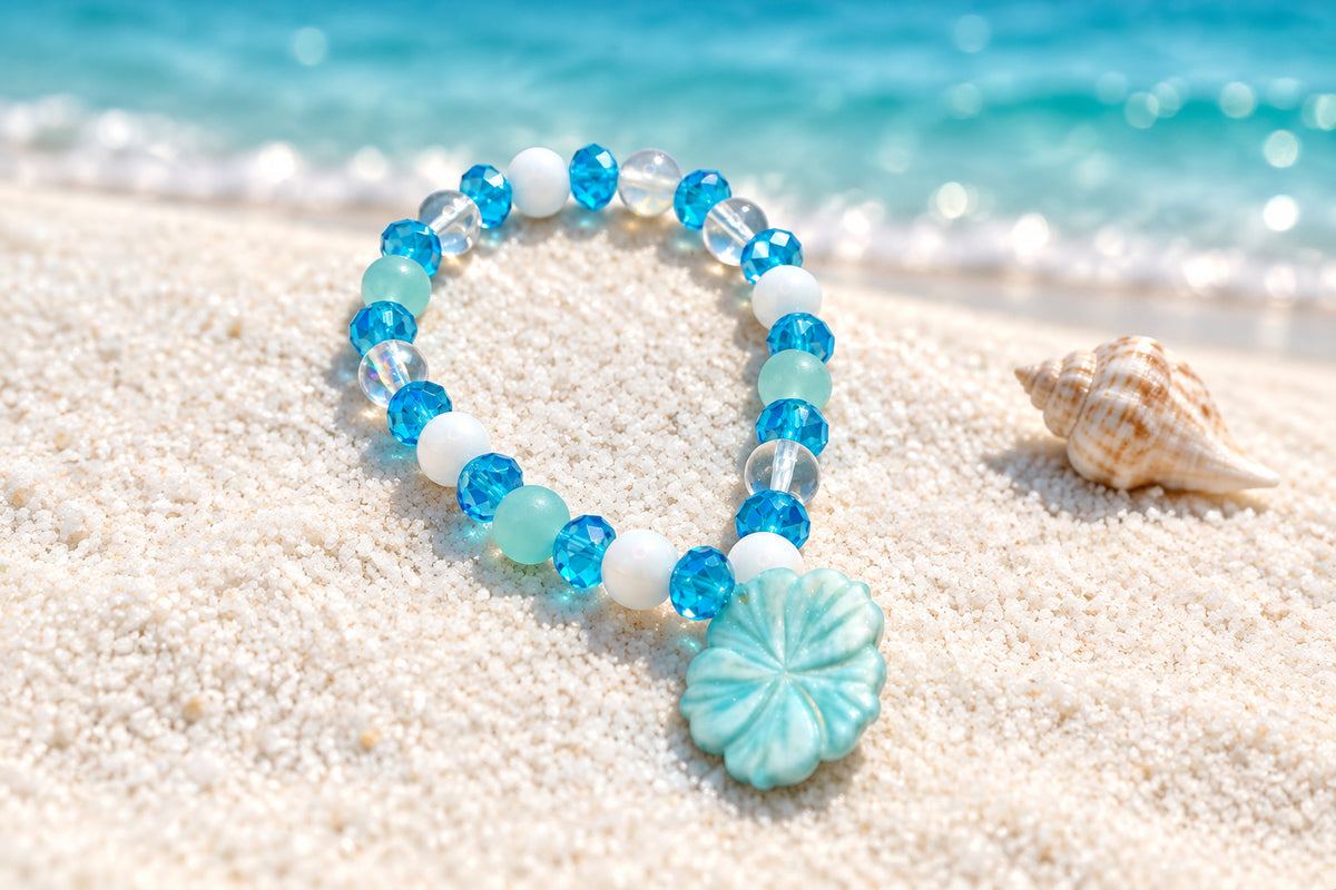 A beaded stretch bracelet featuring light blue, white, and clear faceted beads, with a light blue carved flower charm, displayed on a neutral gray background.