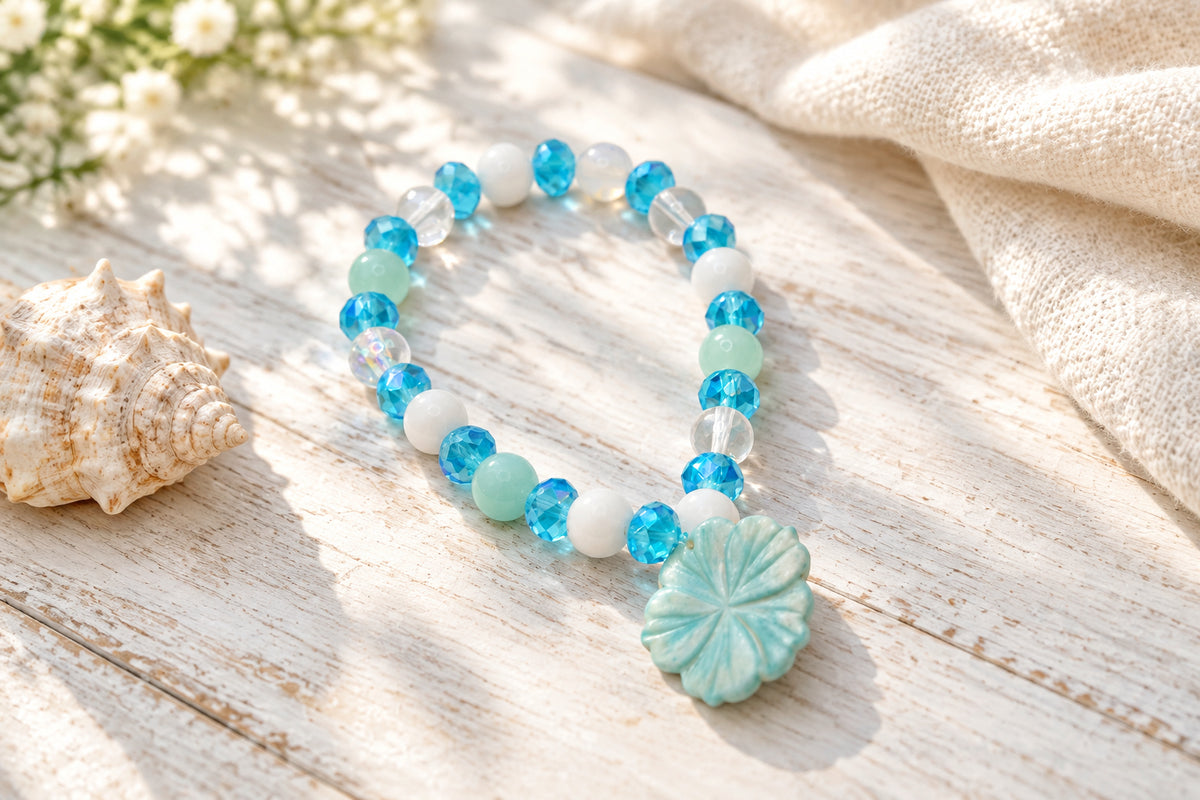 A beaded stretch bracelet featuring light blue, white, and clear faceted beads, with a carved light blue flower-shaped charm, displayed on a neutral gray background.