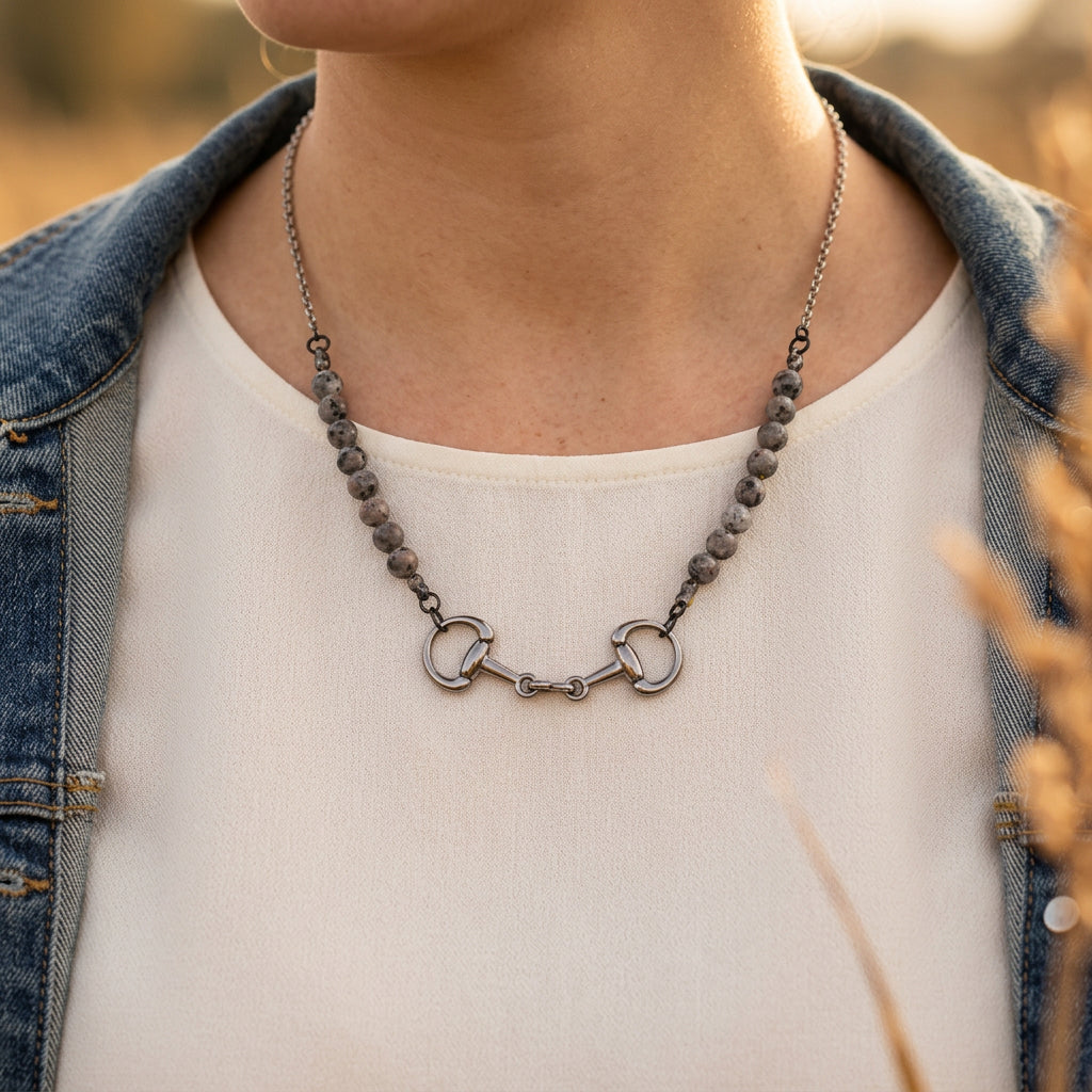 A silver-toned horse bit necklace with gray marbled beads, displayed on a black velvet jewelry bust against a white background.