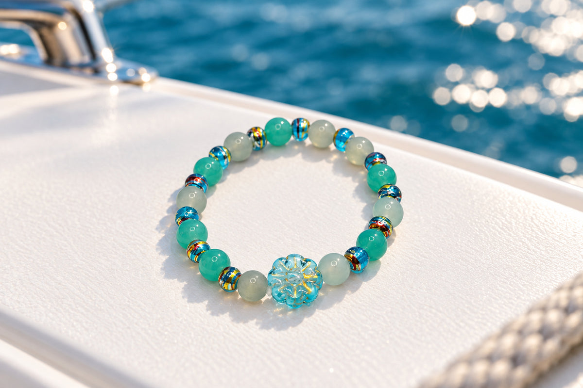 A beaded stretch bracelet featuring light blue, mint green, and gray glass beads, accented with small metallic gold spacers and a central light blue faceted bead, shown on a plain light gray background.