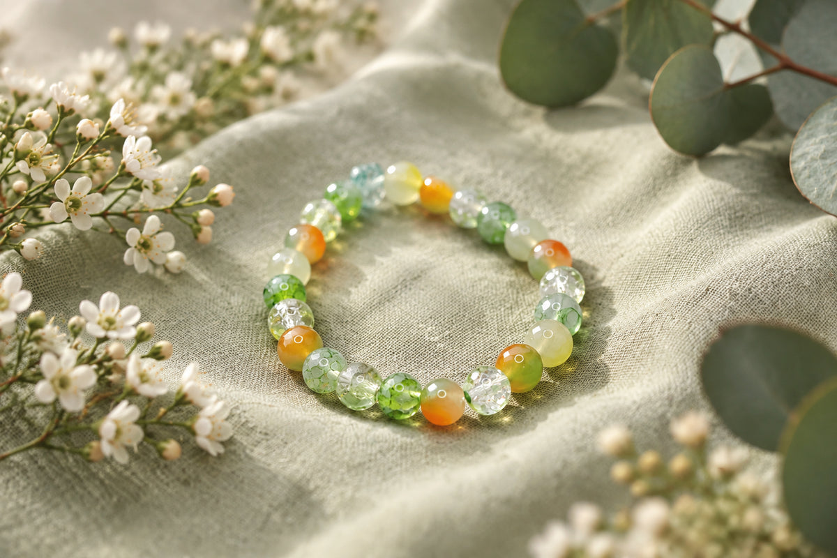 A beaded stretch bracelet made of round glass beads in shades of light green, yellow, and orange, with one small light blue bead at the top, displayed on a plain light gray background.