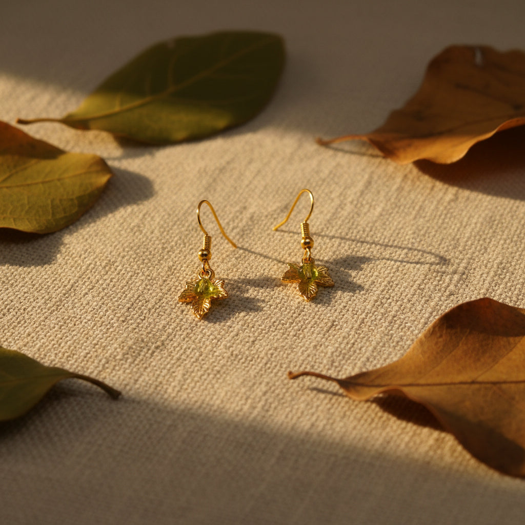A pair of gold leaf dangle earrings displayed on a clear acrylic stand against a neutral gray background.