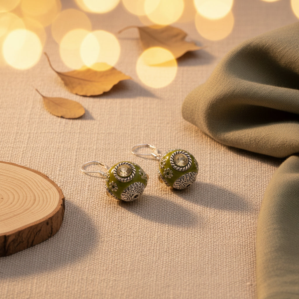 A pair of handmade dangle earrings with olive green enamel and silver filigree, hanging from silver fishhook wires against a light gray background.