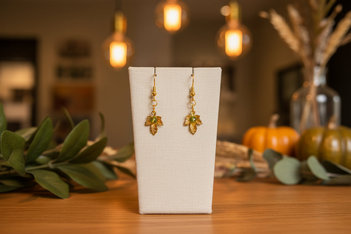 A pair of gold leaf dangle earrings displayed on a clear acrylic stand against a neutral gray background.