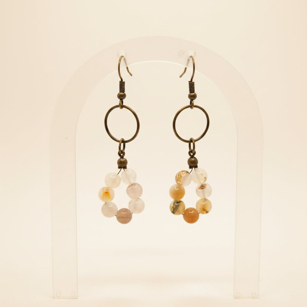 A pair of handmade dangle earrings with dark metal rings and small beads, featuring clear and orange agate-like beads, displayed against a plain white background.