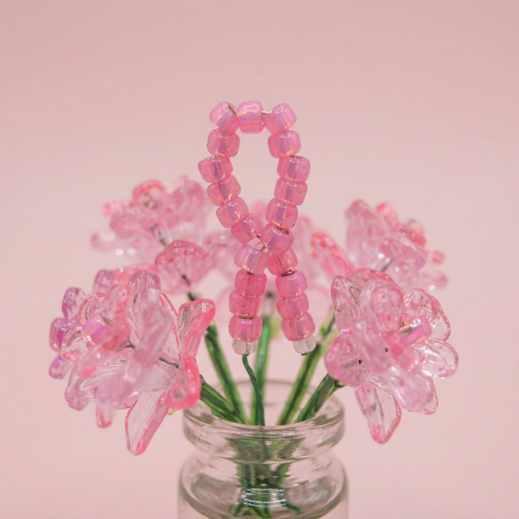 Pink beaded artificial flowers arranged in a small clear glass vase against a plain light gray background.