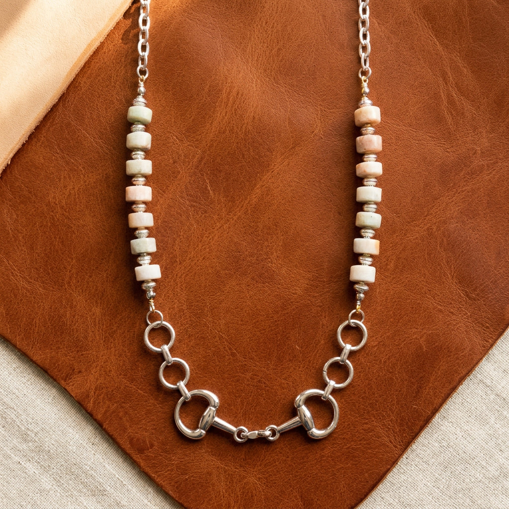A silver-tone necklace with white and peach beads and horse-bit style links, displayed on a black velvet jewelry bust against a white background.