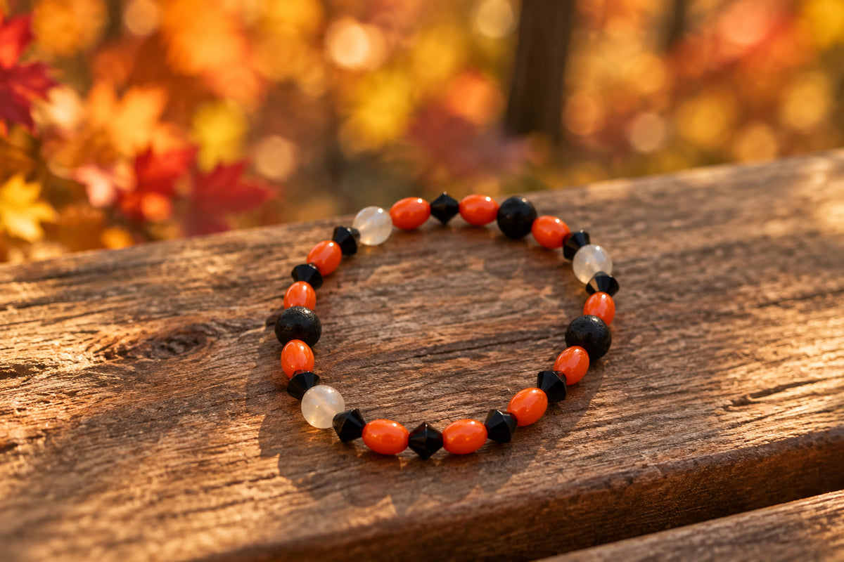 A beaded stretch bracelet featuring alternating orange, black, and white faceted beads, displayed on a plain light gray background.