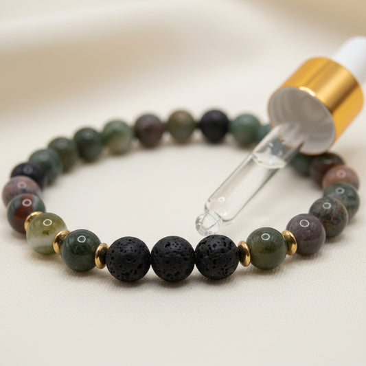 A beaded stretch bracelet made of round dark beads, including black lava stone and green marbled beads, separated by small gold spacer beads, shown on a plain light gray background.
