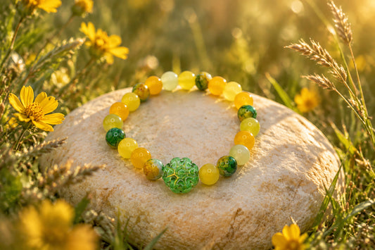 A beaded stretch bracelet featuring yellow and green glass beads, with a textured green central bead, displayed on a plain light gray background.
