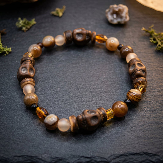 A beaded stretch bracelet featuring carved brown wooden beads, smooth beige agate-like beads, and translucent amber glass beads, arranged in a circle on a light gray background.