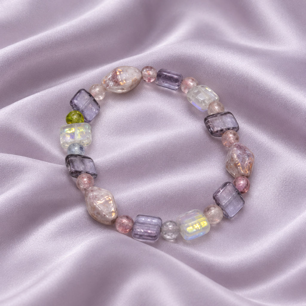A beaded stretch bracelet featuring lavender, pink, and clear glass beads with a small green accent bead, shown on a plain light gray background.