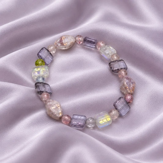 A beaded stretch bracelet featuring lavender, pink, and clear glass beads with a small green accent bead, shown on a plain light gray background.
