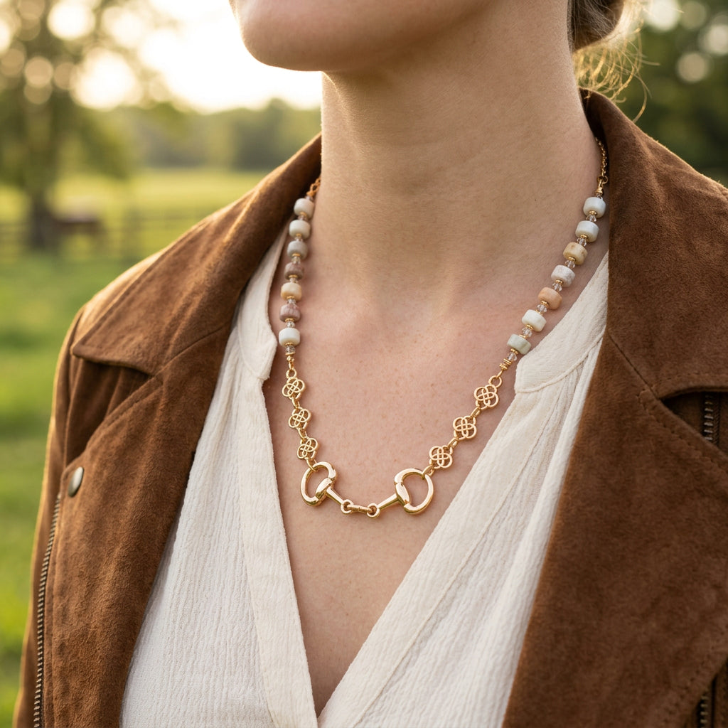 A gold-tone necklace with white and iridescent beads displayed on a black velvet jewelry bust against a white background.