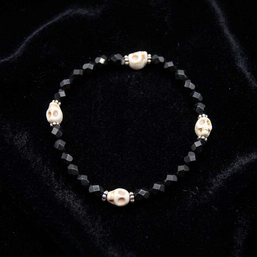 A beaded stretch bracelet featuring faceted black beads and three cream-colored beads with orange and black spots, separated by small silver spacer beads, shown on a plain light gray background.