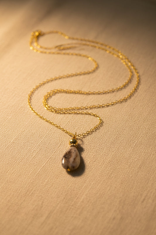 A gold chain necklace with a teardrop-shaped marbled stone pendant, displayed against a plain light gray background.