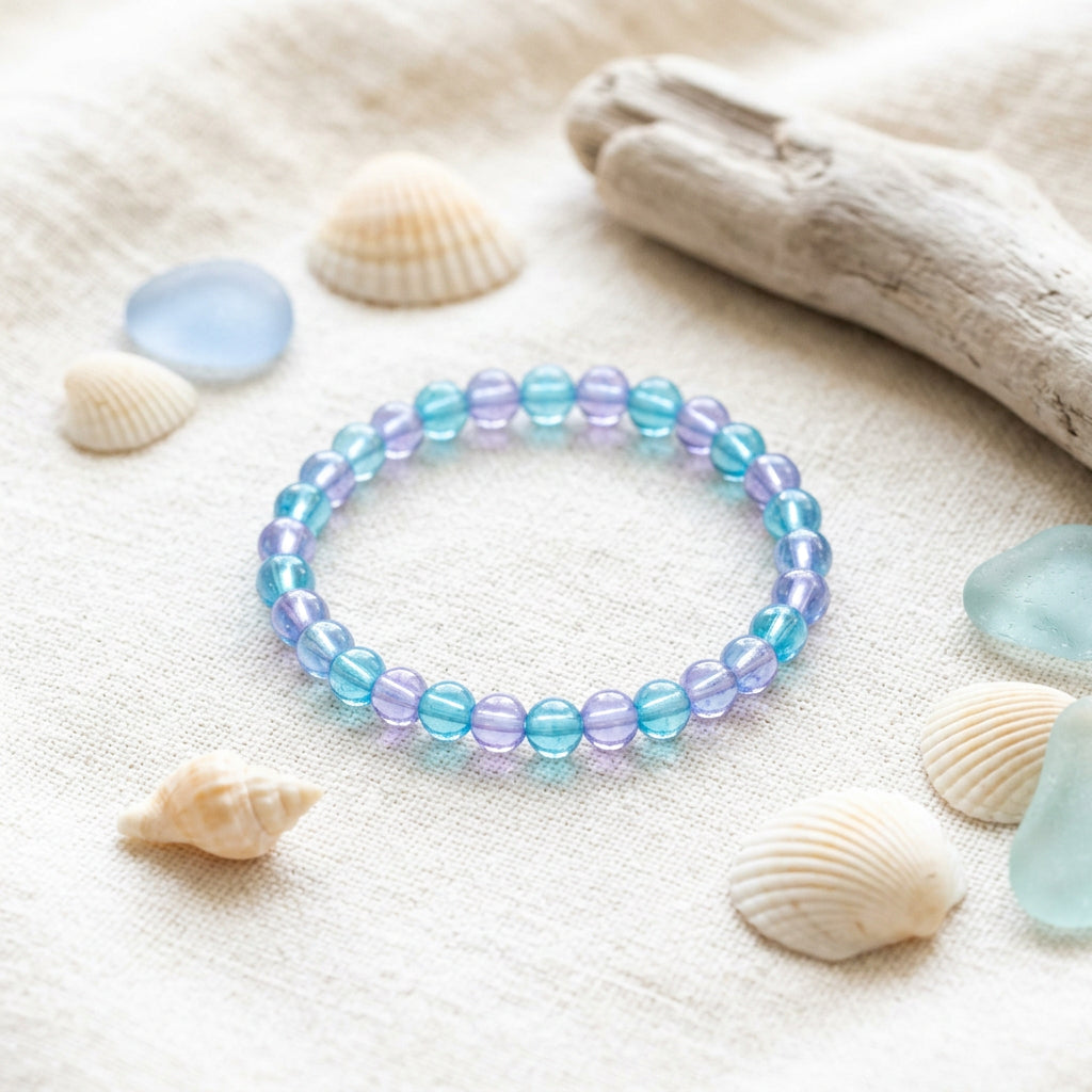 A beaded stretch bracelet made of translucent blue and purple iridescent beads, photographed on a plain light gray background.