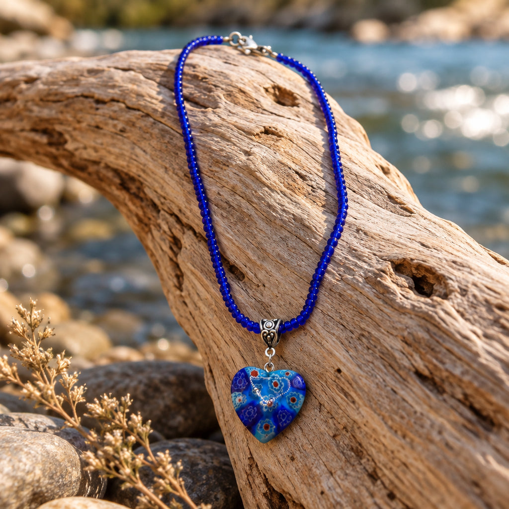 A beaded necklace with a heart-shaped pendant, featuring a vibrant blue beaded chain and a blue and black patterned glass heart pendant with a silver-tone Star of David, displayed on a neutral gray background.