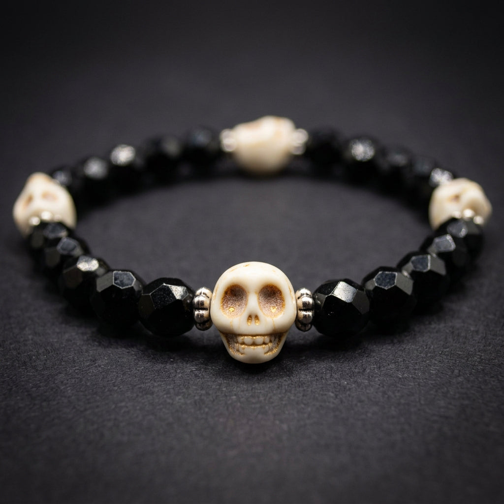 A beaded bracelet featuring faceted black beads and three decorative cream-colored skull spacers with small red and black details, displayed on a neutral light gray background.