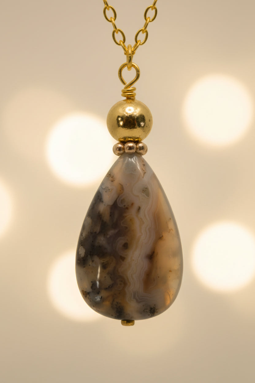 A gold chain necklace with a teardrop-shaped marbled stone pendant, displayed against a plain light gray background.