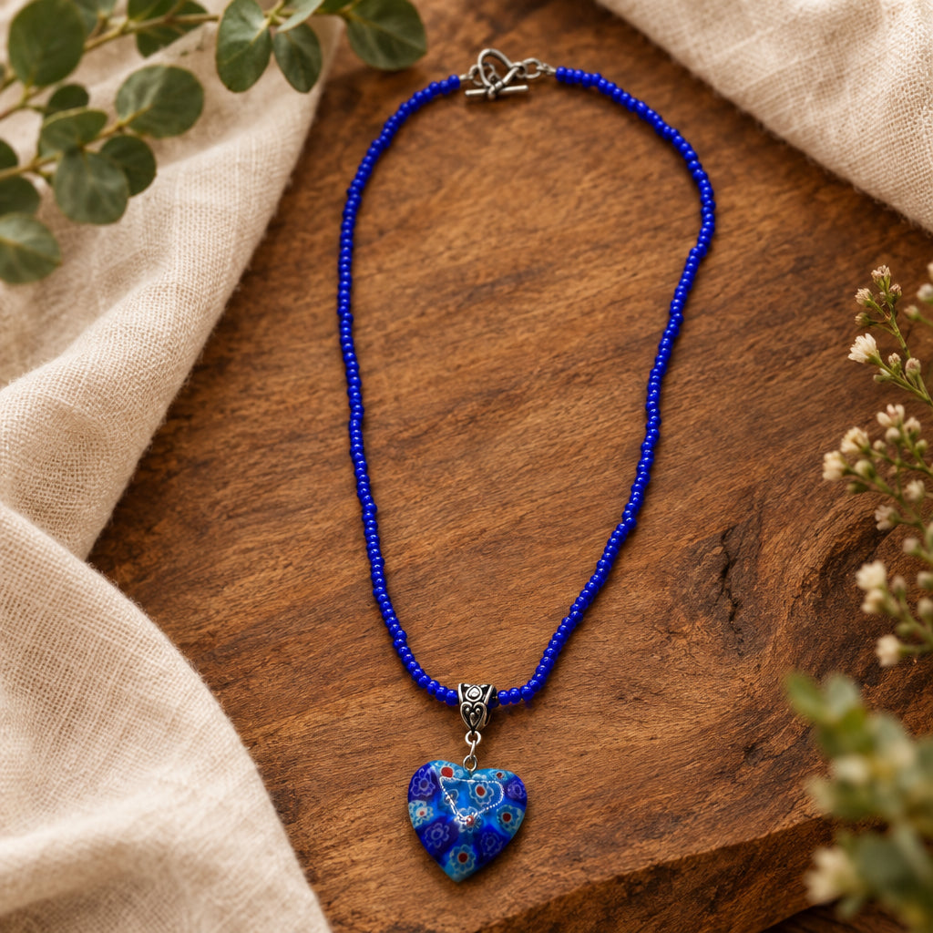 A beaded necklace with a heart-shaped pendant, featuring a vibrant blue cord and a marbled blue and white heart pendant with a silver clasp.