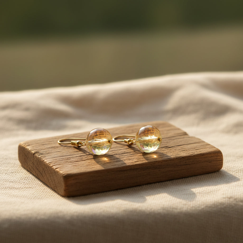 A pair of gold-tone dangle earrings with round, iridescent blue-green opal-like beads, displayed on a clear acrylic stand against a neutral gray background.