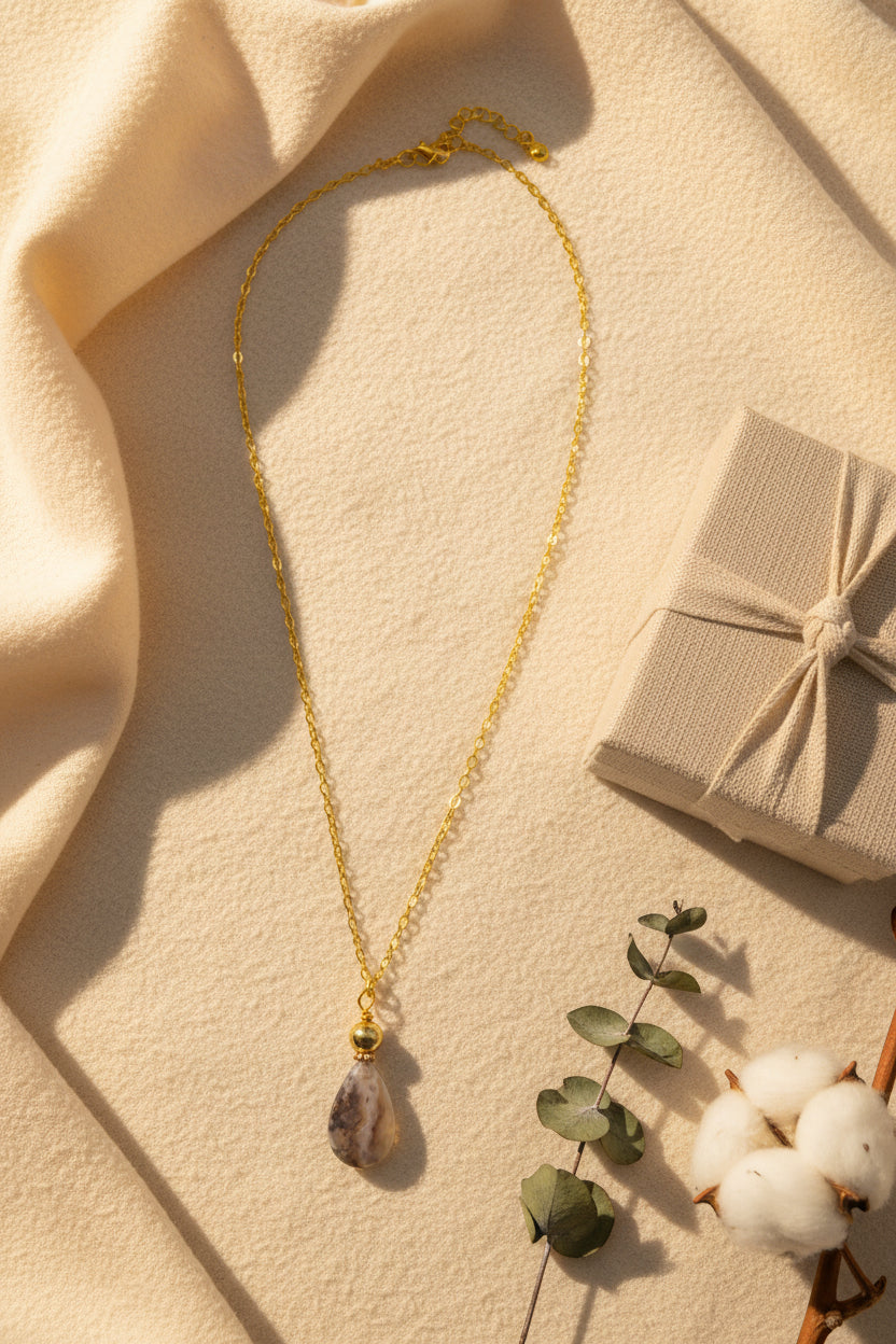 A gold chain necklace with a teardrop-shaped pendant featuring a marbled gray and white stone with gold accents, displayed against a plain light gray background.