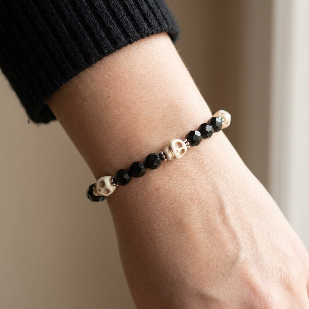 A beaded stretch bracelet featuring faceted black beads and three cream-colored skull accent beads separated by small silver spacer rings, shown on a plain light gray background.