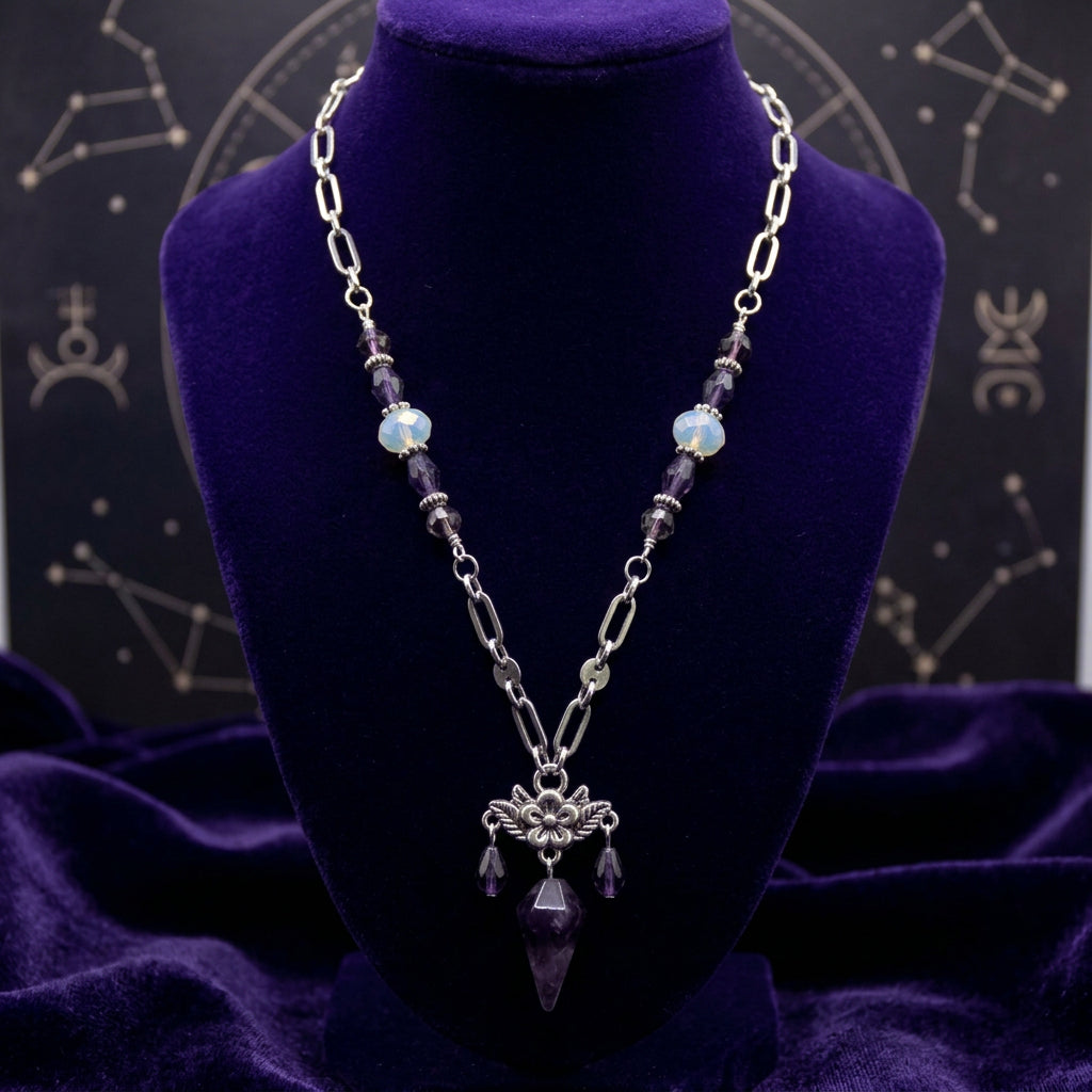 A silver-toned chain necklace featuring dark purple faceted beads and a central ornate pendant with three dangling purple teardrop charms, displayed on a neutral gray background.