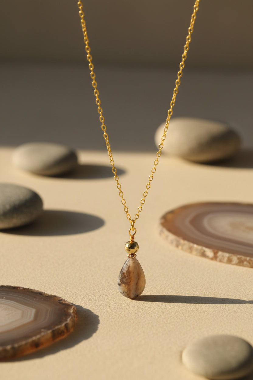 A gold chain necklace with a teardrop-shaped brown and gray marbled pendant, displayed against a plain light gray background.