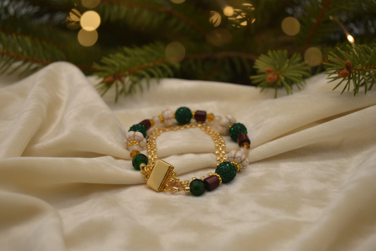A gold-tone beaded bracelet with dark green textured beads, cream-colored beads, and small maroon accents, displayed on a plain light gray background.