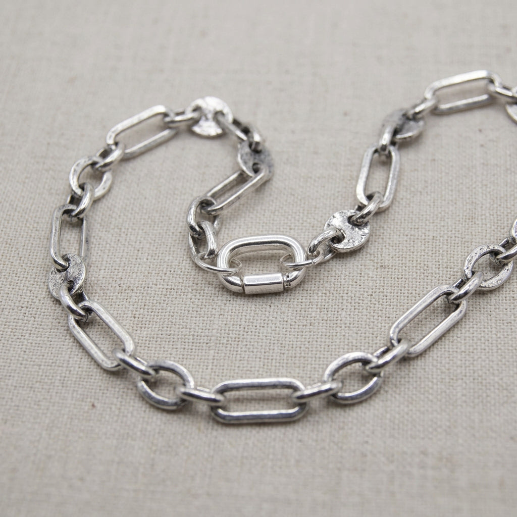 A close-up of a silver-toned metal chain necklace with a central oval clasp and textured links, photographed against a plain light gray background.