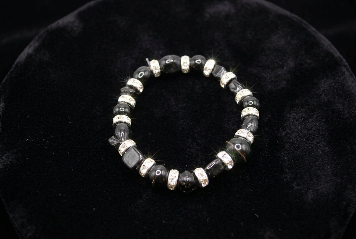A beaded stretch bracelet featuring glossy black round beads and faceted black beads separated by silver-toned spacers with small clear stones, shown on a neutral gray background.