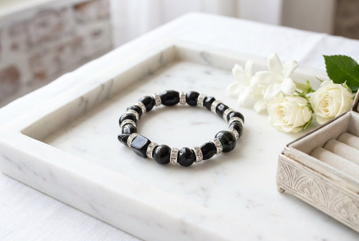 A beaded stretch bracelet featuring glossy black round beads alternating with silver-toned metal spacers that have small clear rhinestones, shown on a neutral gray background.