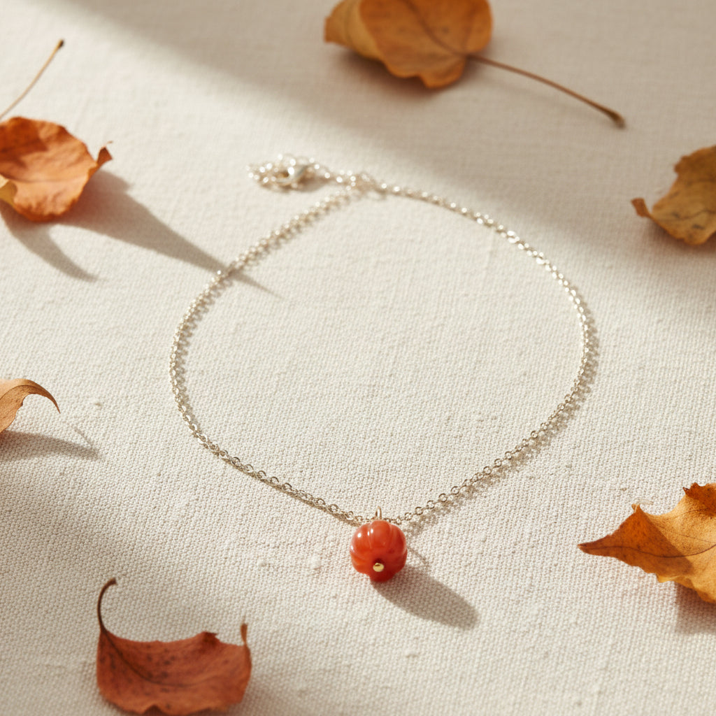 A silver chain necklace with a small round orange pendant, displayed on a black velvet jewelry bust against a white background.