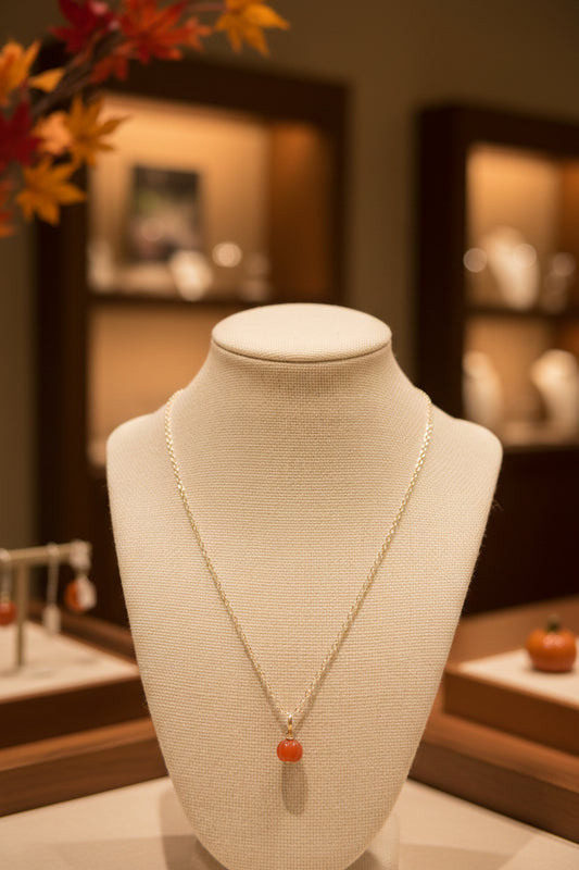 A delicate gold chain necklace with a small round orange bead pendant, displayed on a black velvet jewelry bust against a white background.
