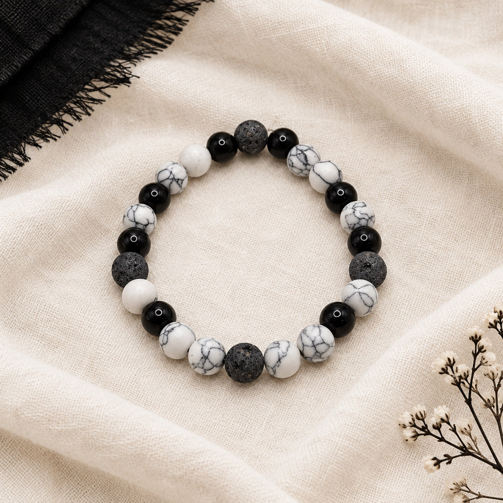 A beaded stretch bracelet featuring alternating black, white, and marbled gray beads, displayed on a neutral light gray background.