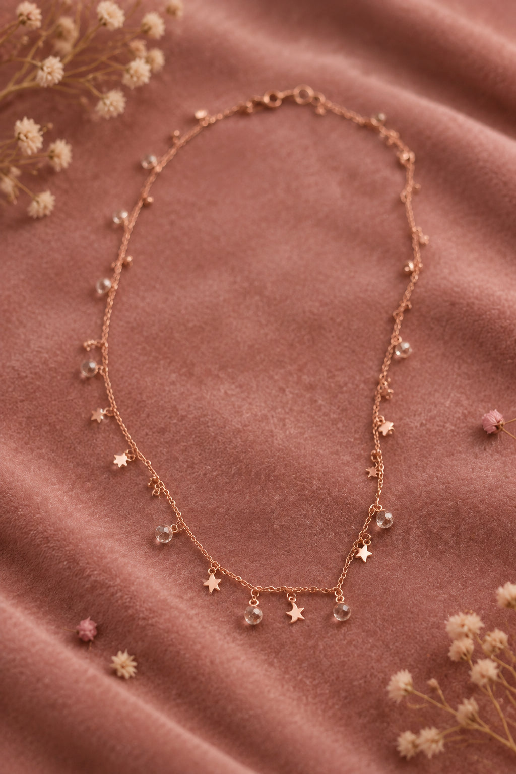 A delicate rose gold necklace with small dangling charms, including stars and crescent moons, laid out on a plain gray background.