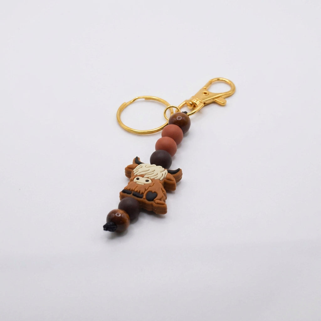 A small beaded keychain or bag charm with gold-tone rings and brown, orange, and cream beads, shown on a plain white background.