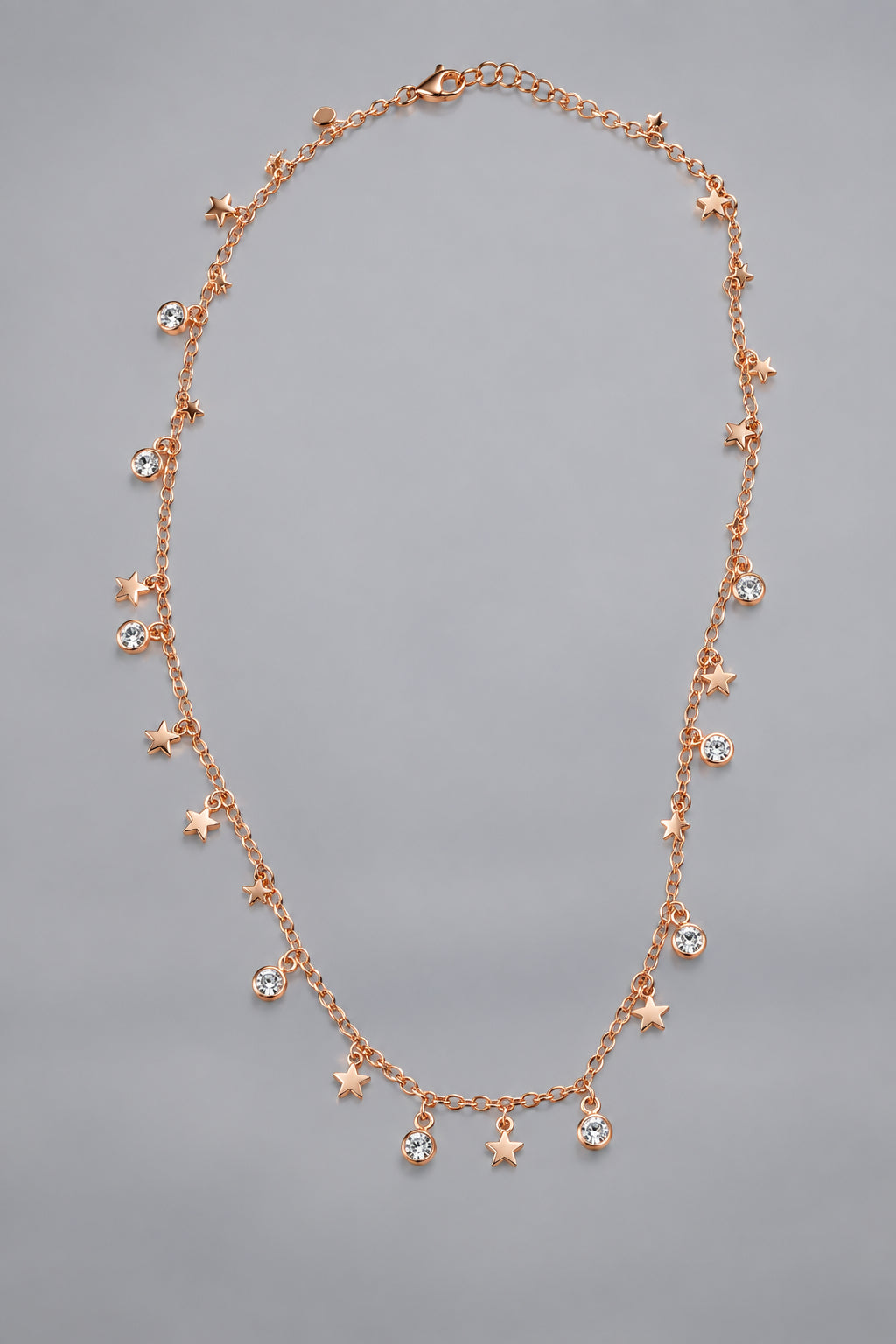 A delicate rose gold necklace with small dangling star and bead charms, displayed on a plain light gray background.