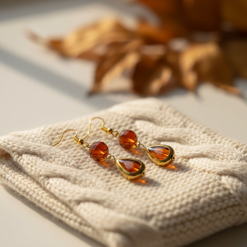 A pair of gold-tone dangle earrings with round amber-brown beads and teardrop-shaped amber drops, displayed on a clear stand against a light gray background.