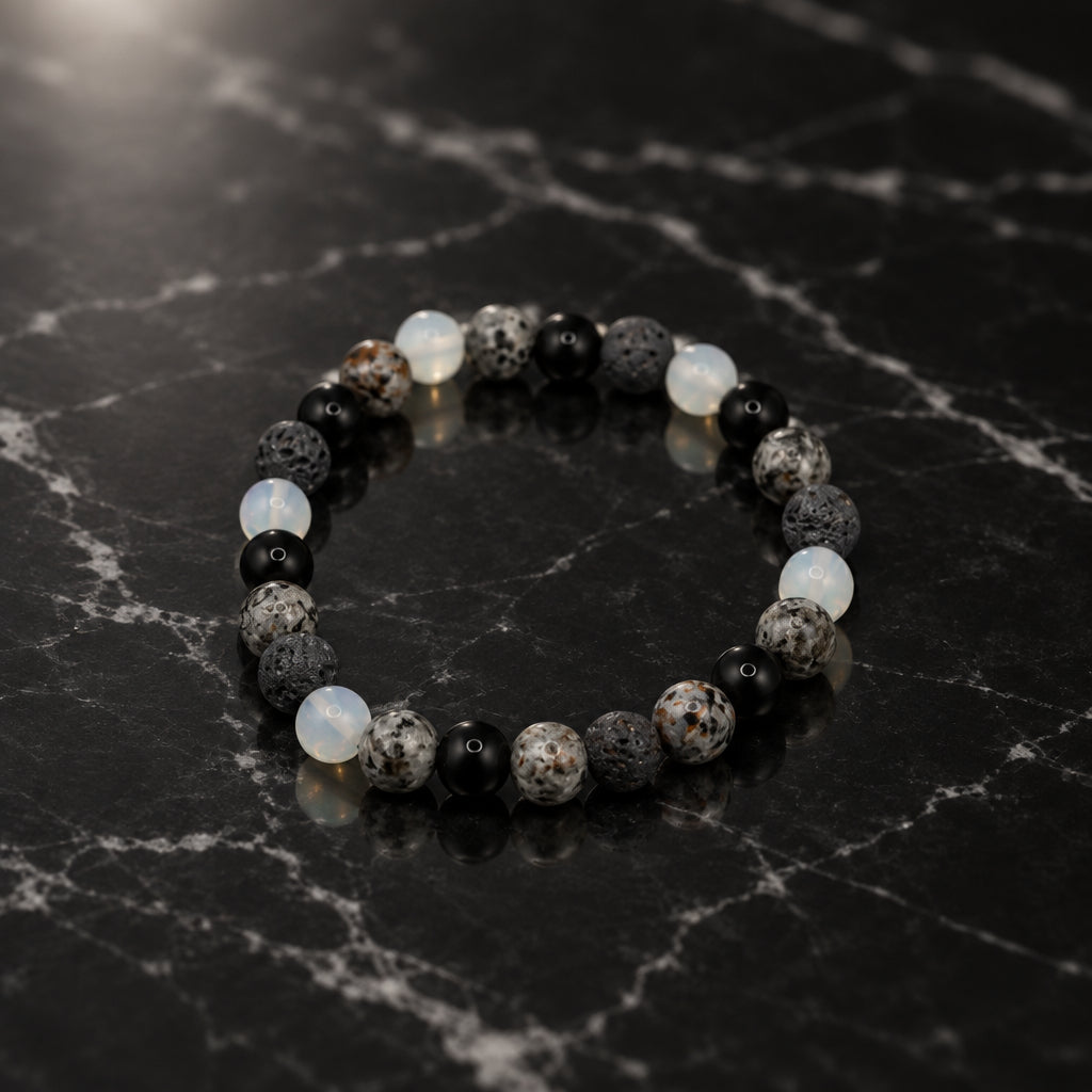 A beaded stretch bracelet made of round dark gray, black, and mottled stone beads, photographed on a plain light gray background.