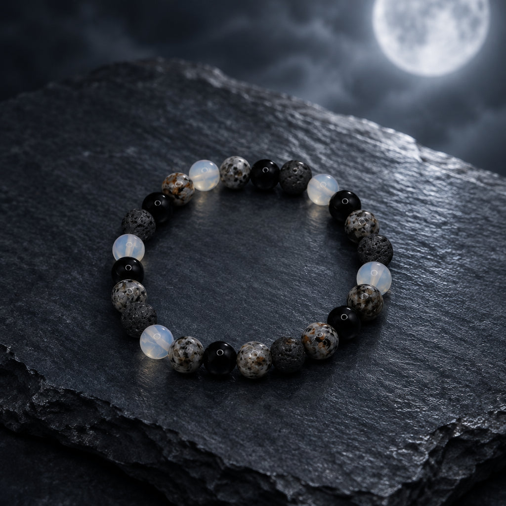 A beaded stretch bracelet made of round dark gray, black, and white marbled beads, displayed on a neutral light gray background.