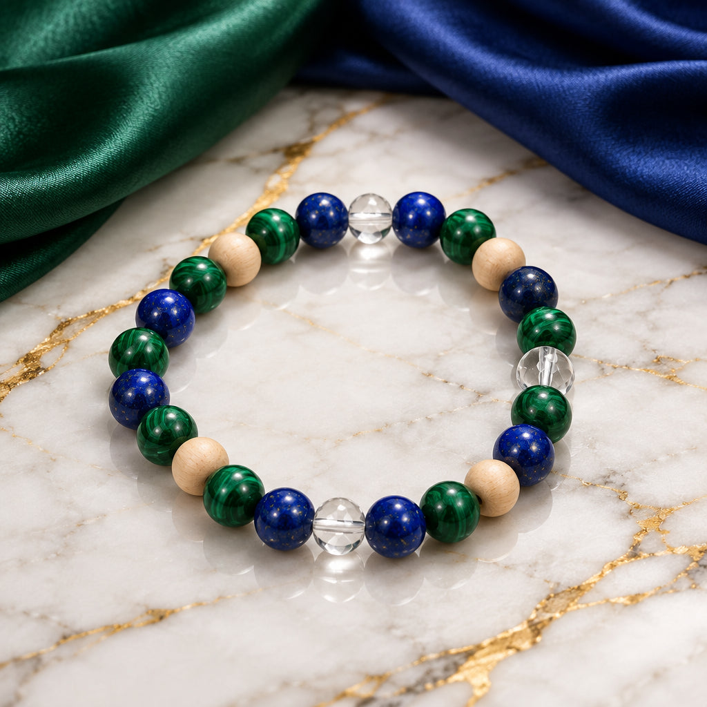 A beaded stretch bracelet featuring dark blue lapis lazuli, emerald green malachite, light beige wooden beads, and a single clear faceted crystal bead, displayed on a neutral gray background.