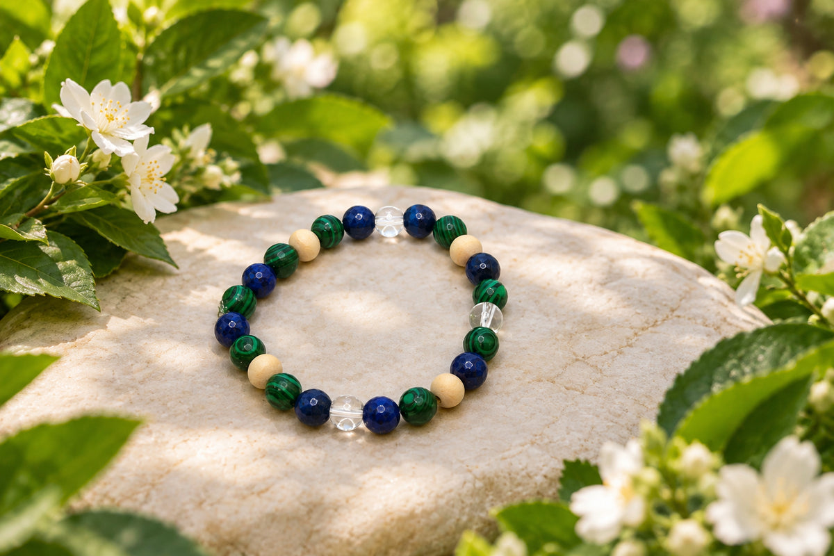 A beaded stretch bracelet featuring dark green, navy blue, light beige, and clear faceted beads, arranged in a circle on a plain light gray background.