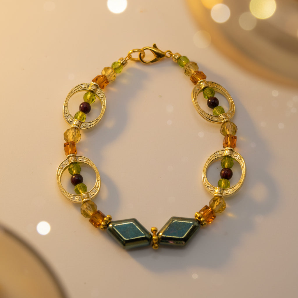 A gold-plated beaded bracelet featuring oval and circular gold spacer rings, small amber-brown and green faceted beads, and two central dark green diamond-shaped beads, displayed on a neutral gray background.