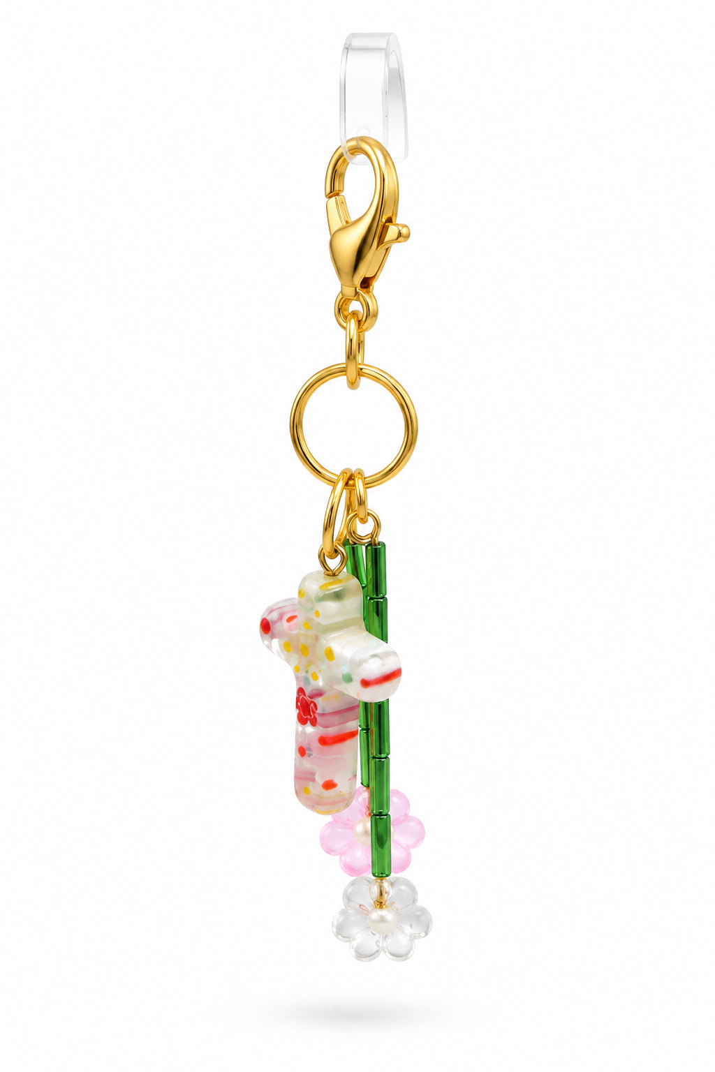 A small gold-tone keychain or bag charm with a floral and green patterned dangling figure, displayed on a clear acrylic stand against a light gray background.