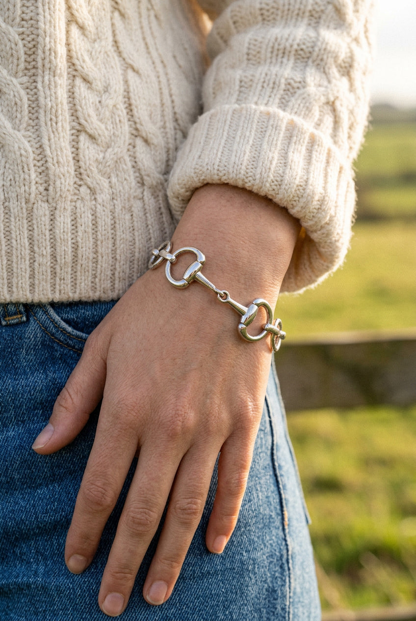 A silver-tone metal bracelet featuring a horsebit clasp closure, circular link chain, and a central decorative oval charm, shown on a plain light gray background.