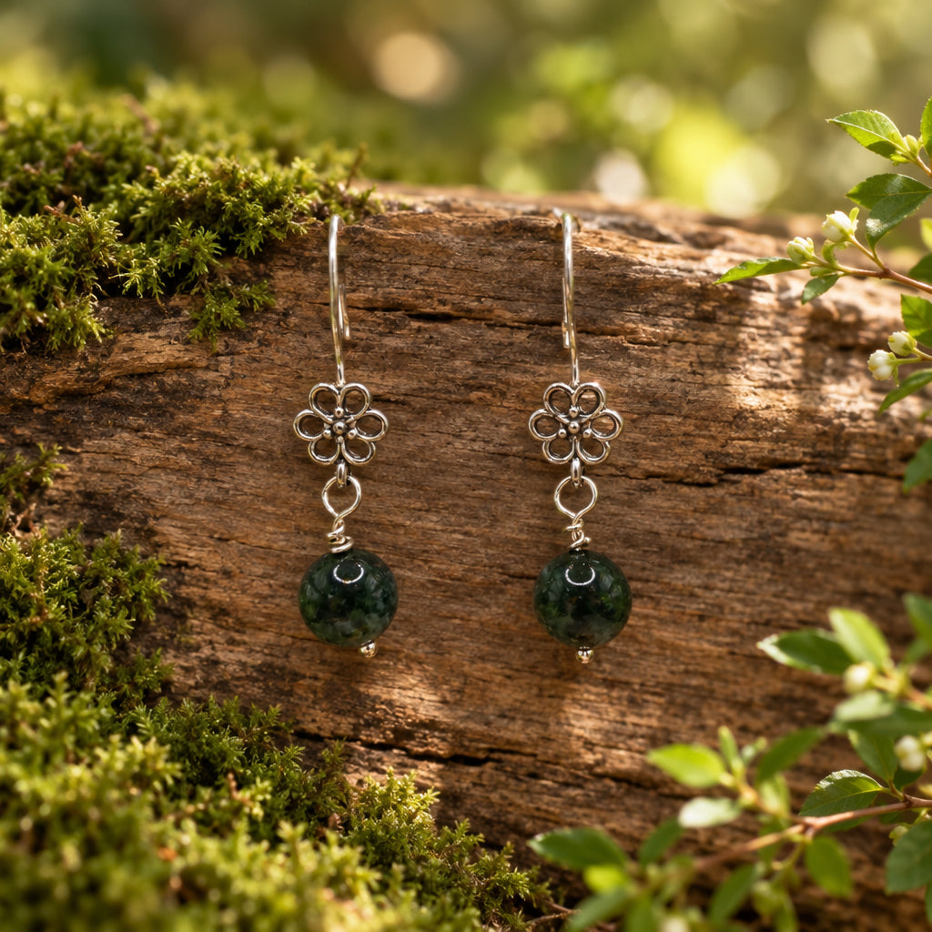 A pair of silver-toned dangle earrings with a floral filigree top and a round dark stone bead below, displayed on a clear acrylic stand against a light gray background.